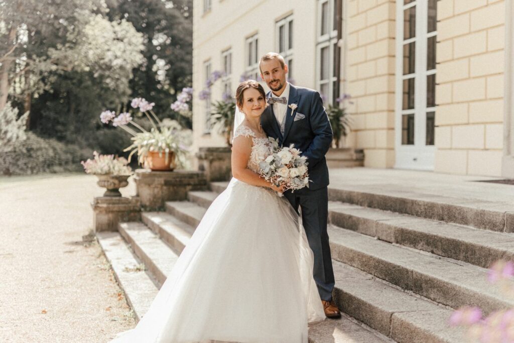 Hochzeitspaar traut sich im Barocken Stil in einem Gut. Beide schauen verliebt in die Kamera