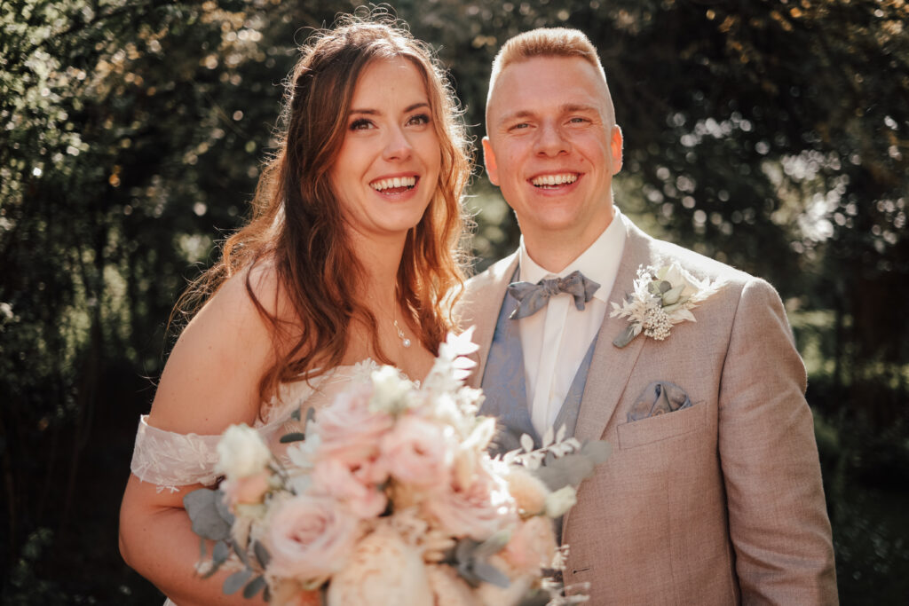 Tolle Hochzeitsfotografie in der Nähe von Rostock - Brautpaar lächelt. Die Braut trägt einen Blumenstrauß