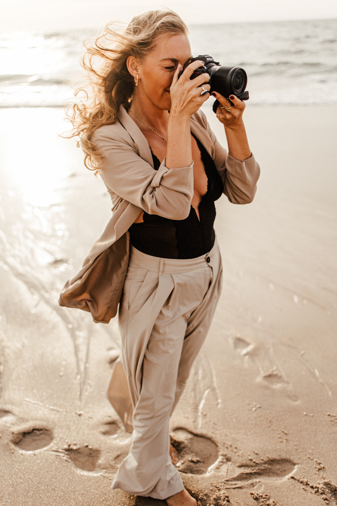 Personal-Branding-Fotografie am Nordseestrand von Sylt für dein erfolgreiches Business. Frau spaziert am Strand mit ihrer Kamera. im Hintergrund geht die Sonne unter.