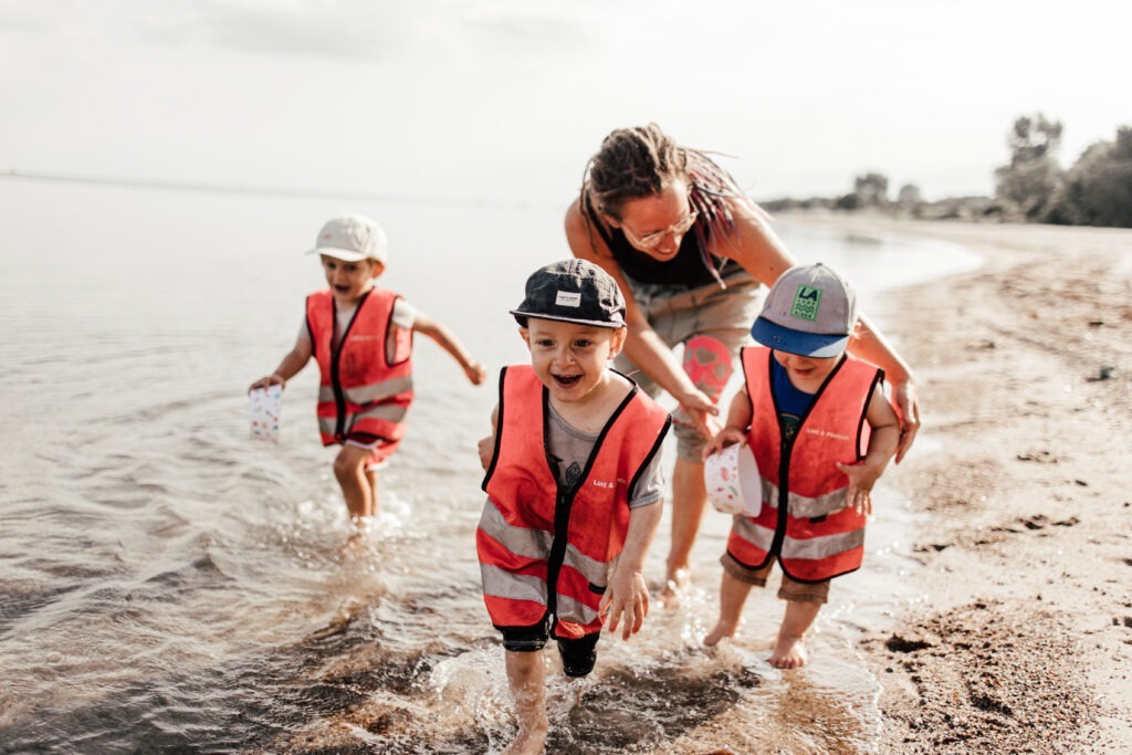 Startseite 17 Kinder machen einen Ausflug an den Strand mit ihrer Tagesmutter. Die Kinder haben Spaß.