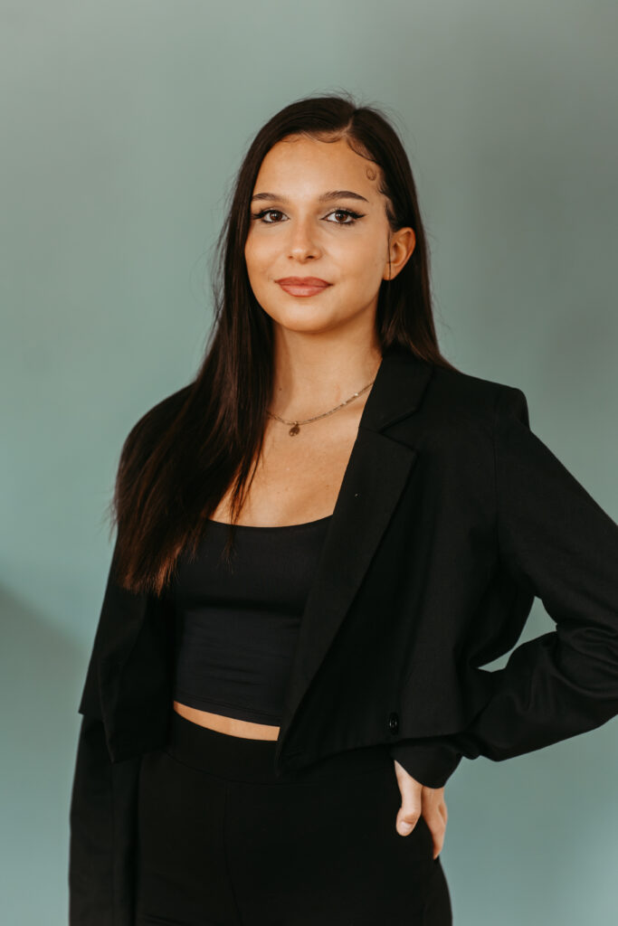 Junge Frau lächelt in die Kamera vor einem blauen Hintergrund.