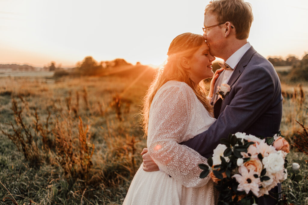 Hochzeitsfotograf und Hochzeitsvideograf in Schleswig-Holstein. Braut und Bräutigam stehen in der freien Natur auf einer Wiese bei Sonnenuntergang.