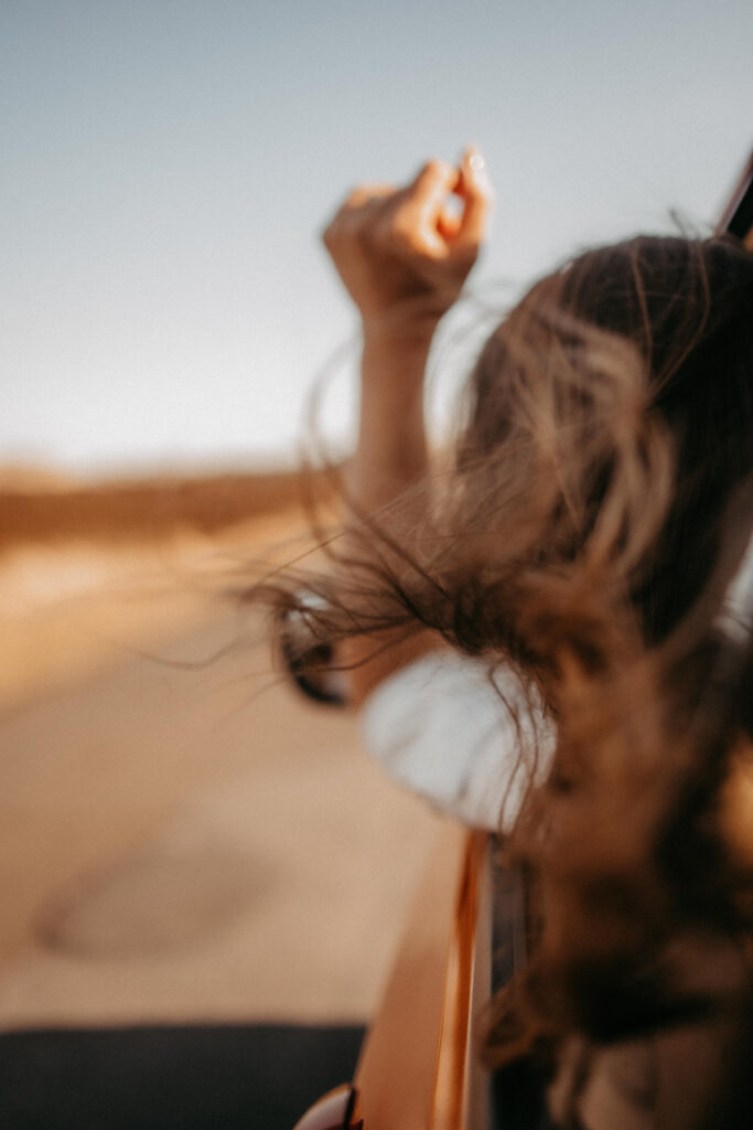 Eine Frau streckt beim Autofahren auf Sylt den Arm aus dem Fenster, der Wind weht durch ihr Haar. Die Szene vermittelt Freiheit und Reiselust – typisch für Sylt-Travel-Erlebnisse.