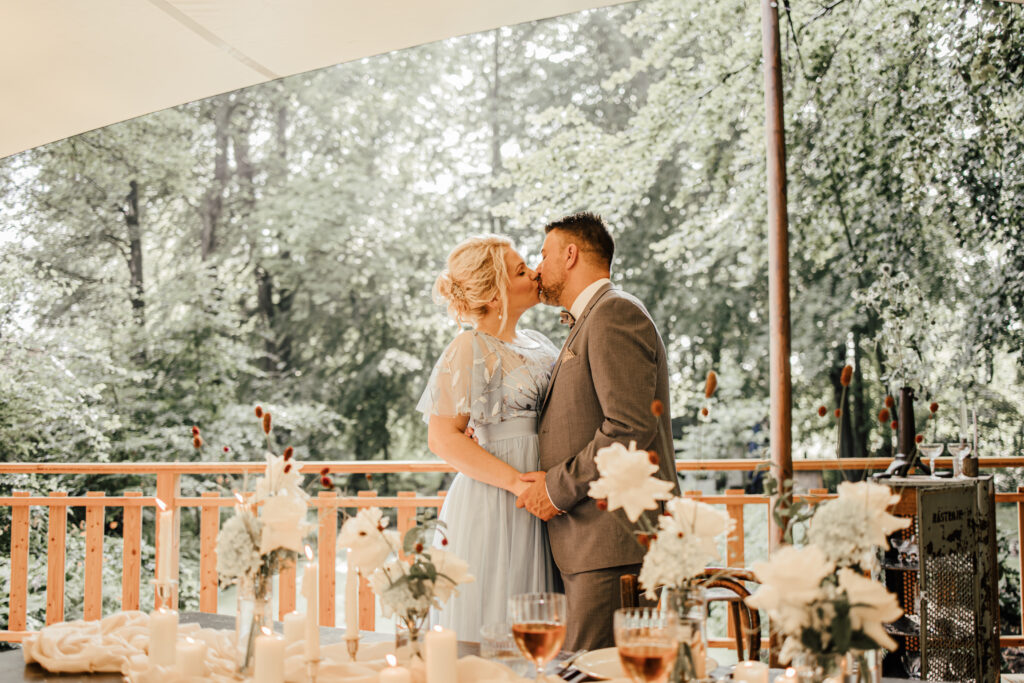Das glückliche Ehepaar küsst sich und steht dabei neben der gedeckten Tafel.