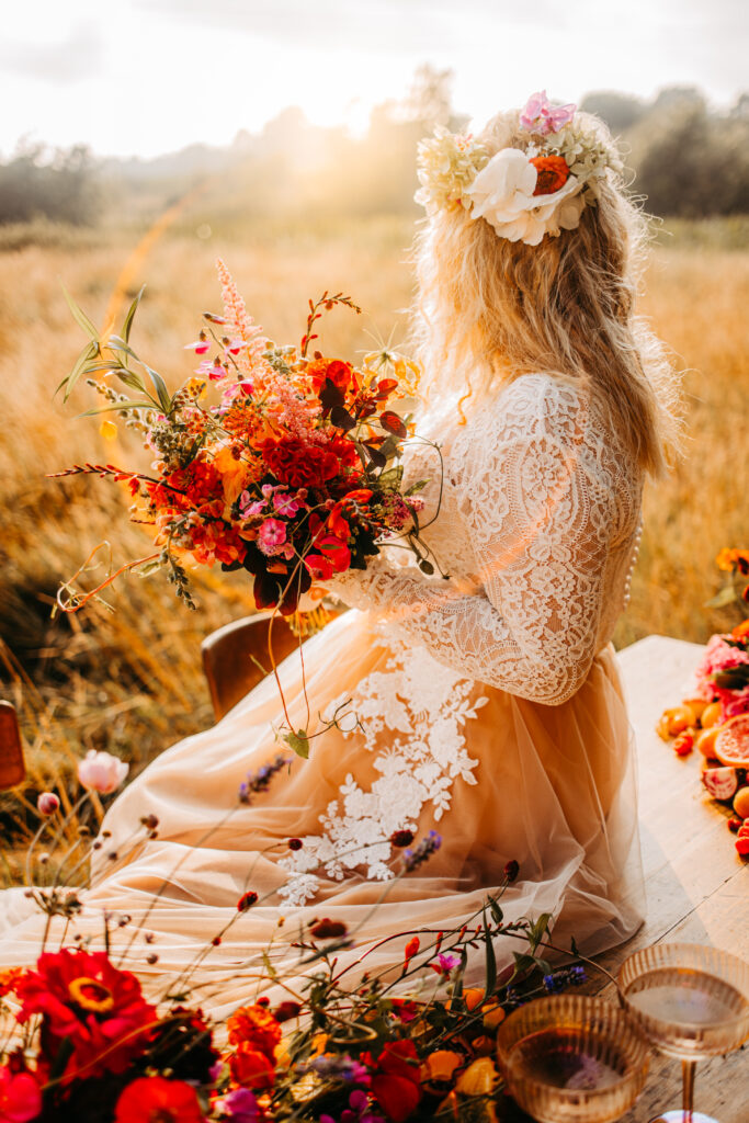 Eine glückliche Braut sitzt auf der Decke zwischen Blumen.