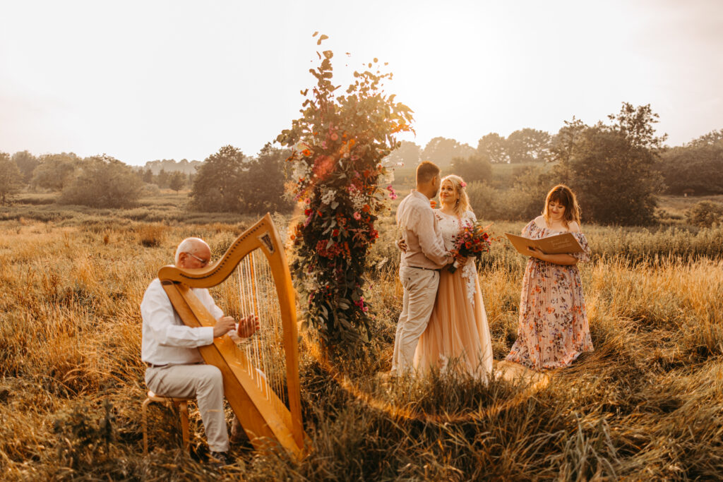 Ein Ehepaar während der Trauung auf einer Blumenwiese mit musikalischer Begleitung einer Harfe.